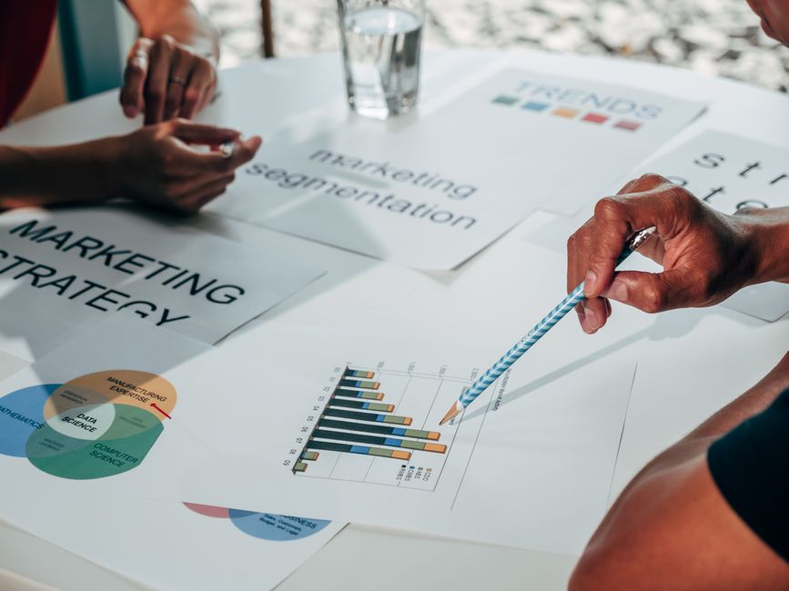 Team members review marketing strategy documents with bar and pie charts on a white table.