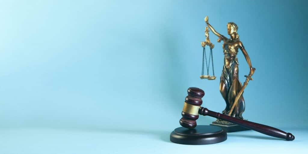 Statue of Lady Justice holding scales and a sword with a gavel in the foreground, symbolizing law and justice set against a blue backdrop